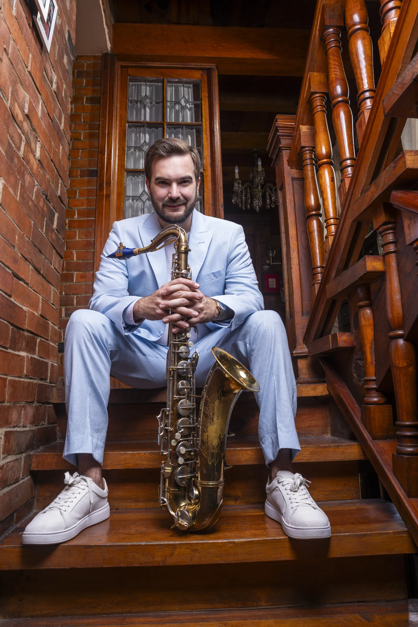 Lorenzo Ferrero seated on stairs in a blue suit with his saxophone