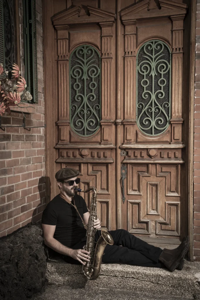 Lorenzo Ferrero with his saxophone beside a carved wooden doorway